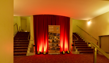 Majestätischer Eingang zum Saal mit angestrahltem LUX-Poster.