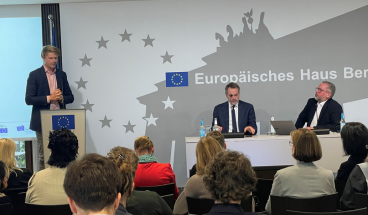 Armin Steuernagel von der Stiftung Verantwortungseigentum kommentiert vor Publikum auf dem Podium das "28. Regime". MdEP René Repasi und Moderator Bernd Hüttemann  von der EBD hören zu.