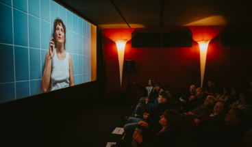 Kinosaal mit Publikum und Ausschnitt von Love me tender auf der Leinwand.